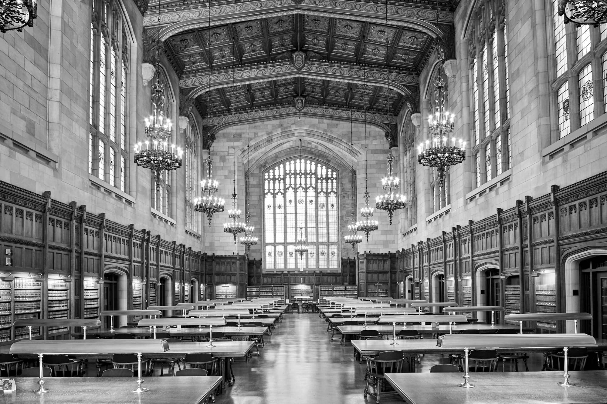 Grand library reading room with long wooden tables and tall bookshelves